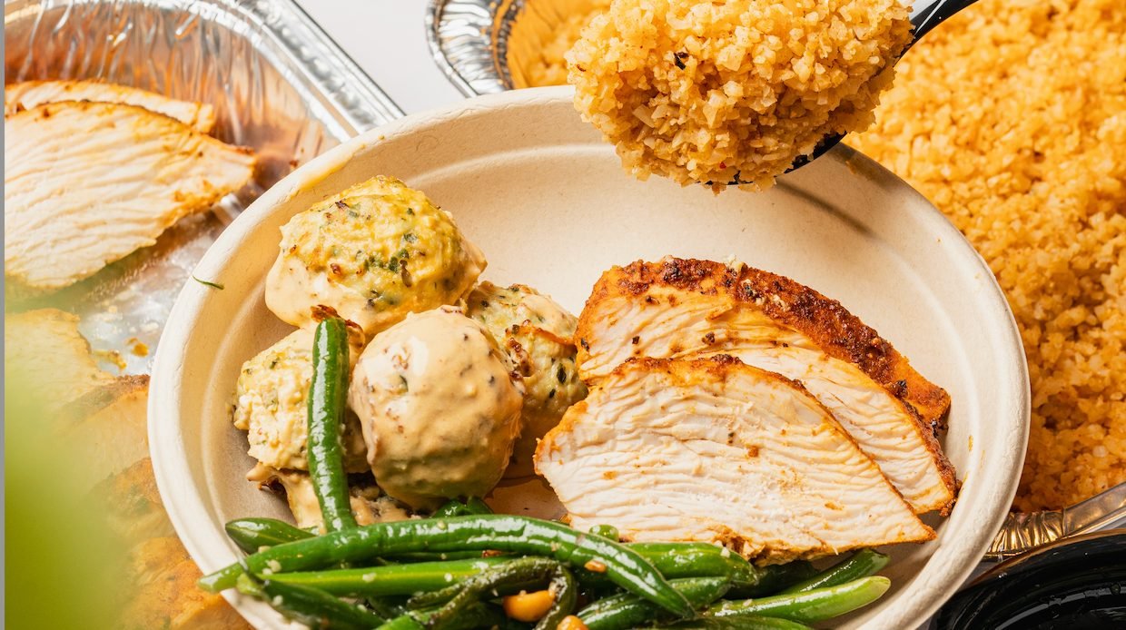 A Vale bowl of sliced roasted chicken, meatballs and green beans beside catering trays of Vale rice